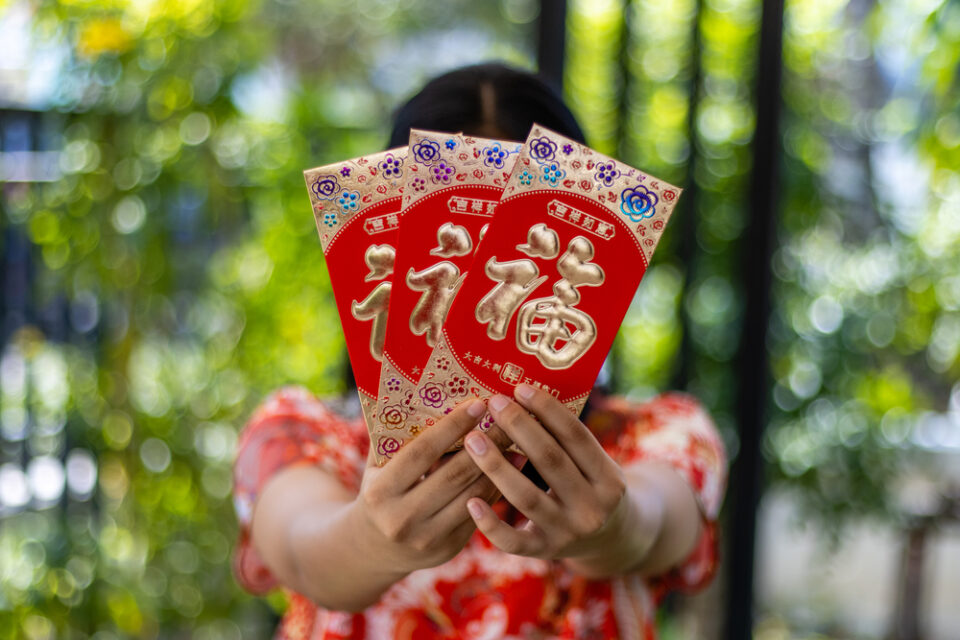 A woman holding three red envelopes decorated with gold Chinese characters.