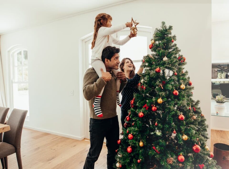 A family putting up their Christmas tree. A father has his daughter on his shoulders to put the star on top