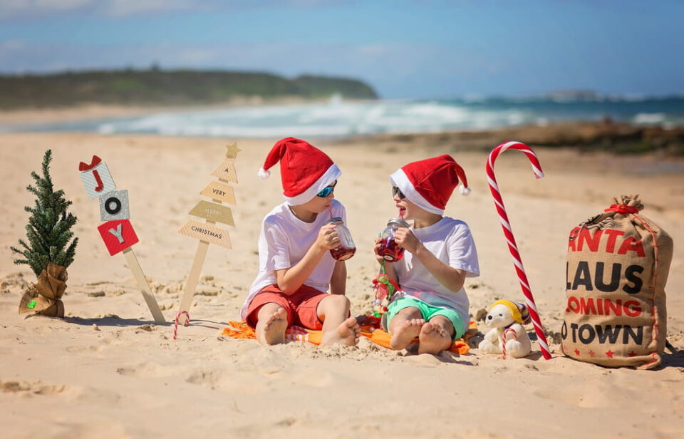 Two children in Christmas hats celebrate on a sunny beach