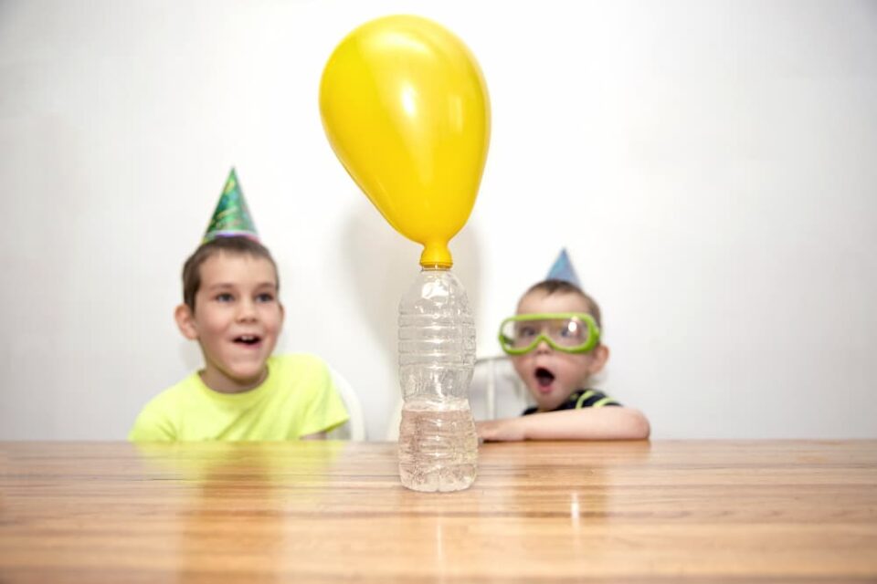 Kids watching a balloon inflate on top of a plastic bottle