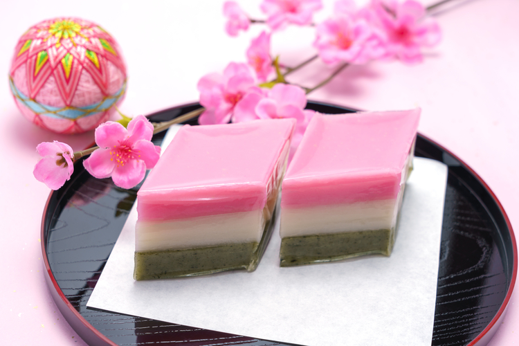 Two pieces of hishi mochi on a plate with cherry blossoms