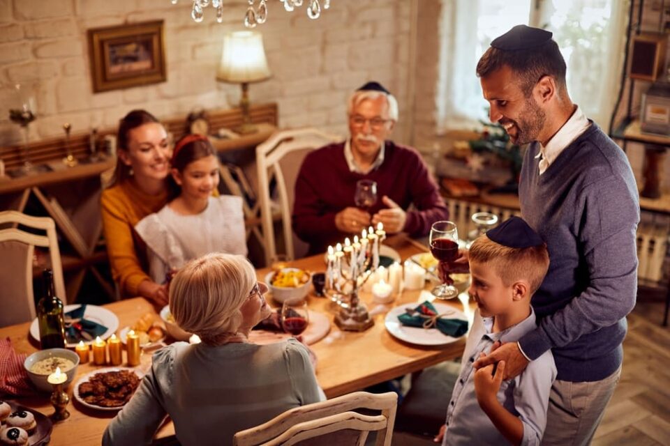 A multigenerational Jewish family sits down to Hanukkah dinner with a menorah on the table