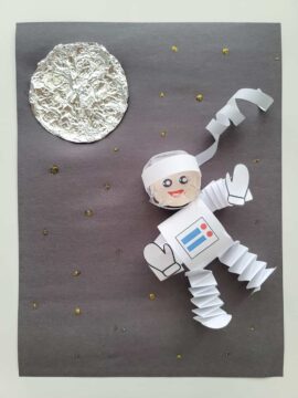 Completed astronaut craft, with paper astronaut, aluminum foil moon, and gold stars on black construction paper