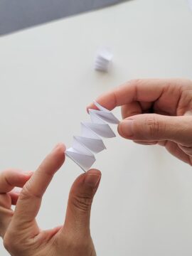 Hands showing a completed accordion fold on a strip of paper