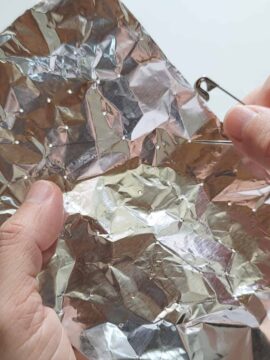 Person making holes in aluminum foil with safety pin