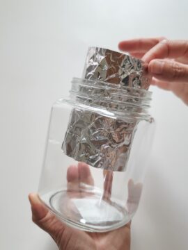 Person rolling aluminum foil into a mason jar for constellation light