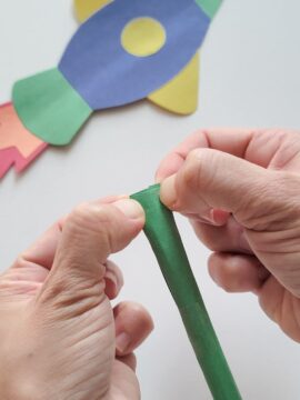 Person pinching shut construction paper tube for straw rocket