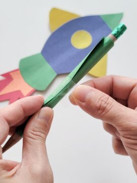 Person taping together a construction paper tube around a pencil