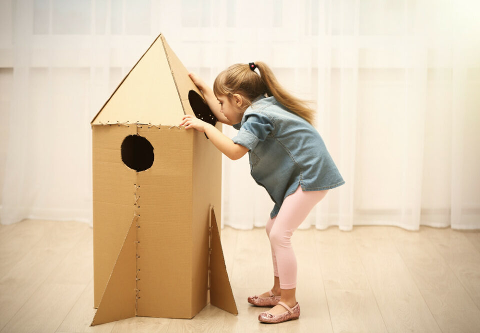 A-little-girl-playing-with-a-DIY-toy-spaceship-made-out-of-a-recycled cardboard-box