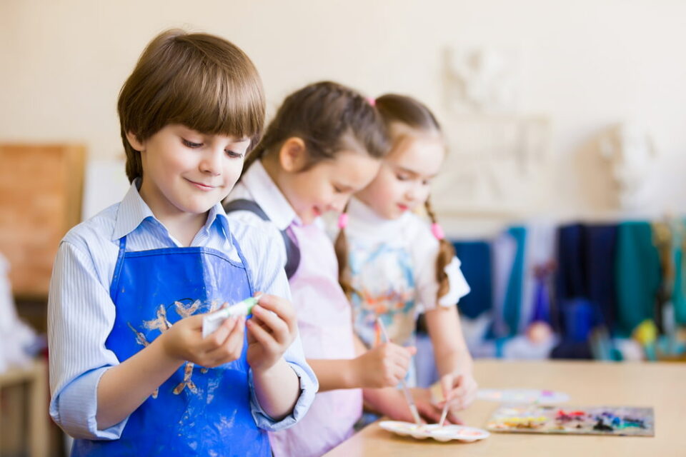 Three children having fun playing with paints together.