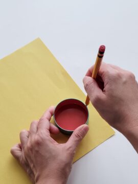 Person drawing circles on yellow paper using stencil