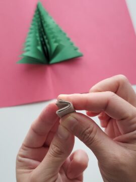 Person folding cardboard to make the trunk of a pop-up Christmas tree card