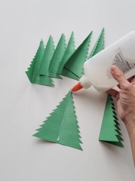 Person putting glue in crease of folded paper Christmas tree