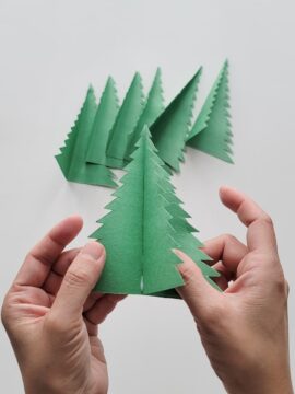 Person gluing a second folded paper Christmas tree inside of the first