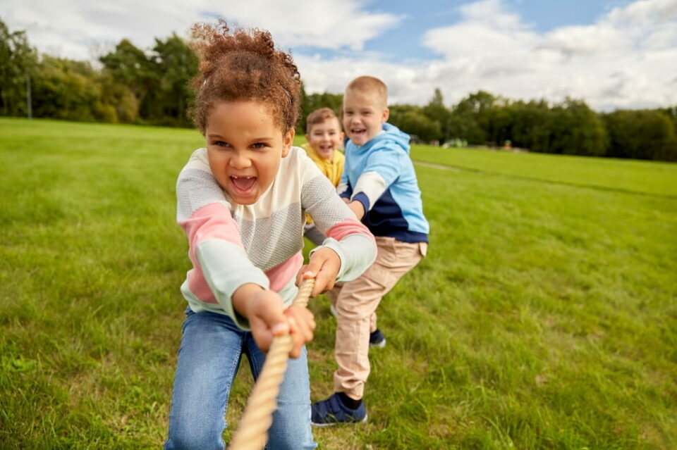 Group of happy kids playing tug-of-war game at park