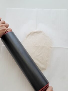 Person rolling out salt dough between two sheets of parchment paper to make holiday ornaments