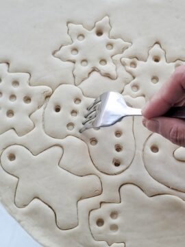 Person adding texture to unbaked holiday salt dough ornaments using a fork