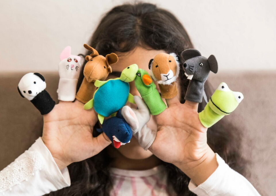 Young child covering face wearing animal puppets on fingers
