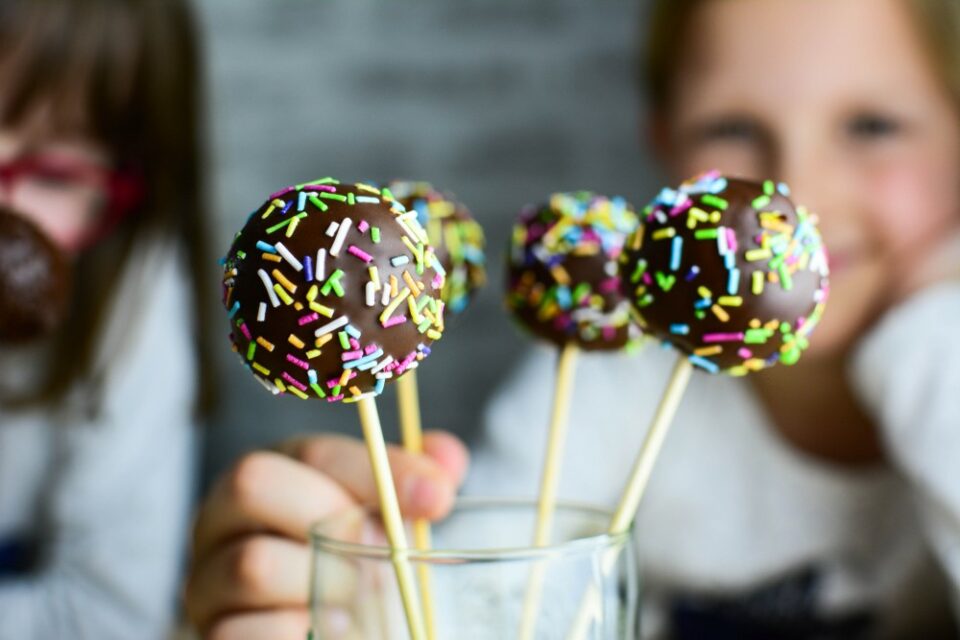 A young girl picking up a chocolate-coated cake pop decorated with sprinkles