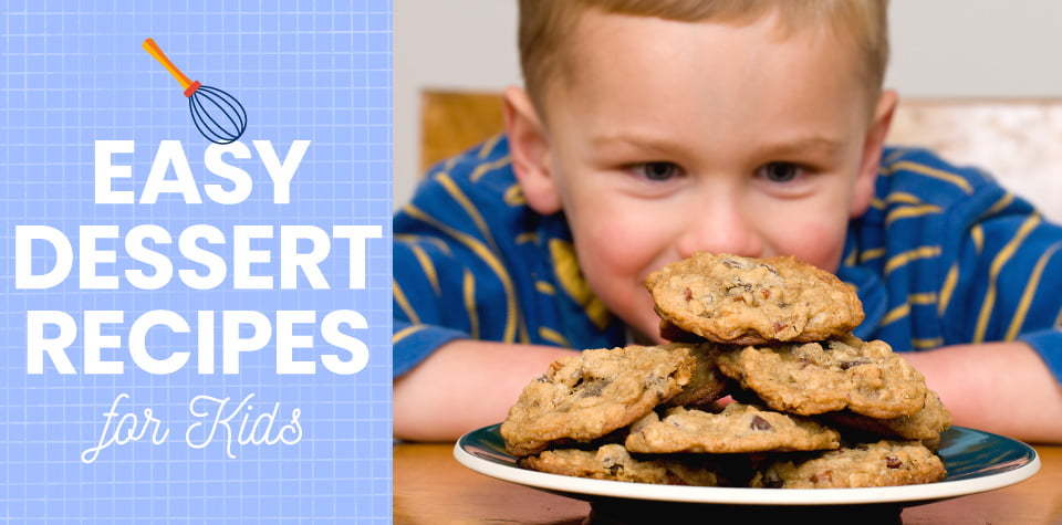 A boy looking eagerly at a plate heaped with cookies in front of him