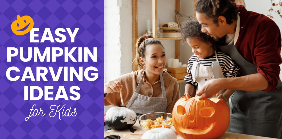 A young boy with his parents smiling and carving a Halloween pumpkin in the kitchen