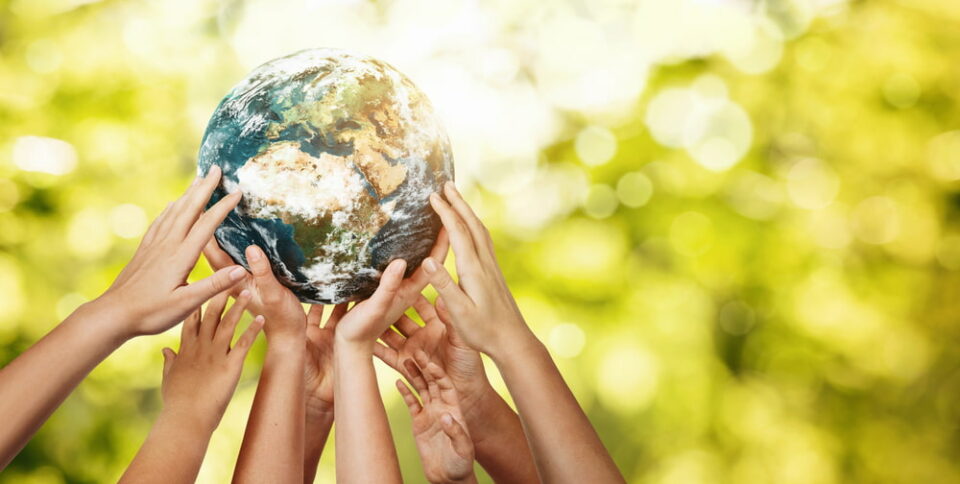 Photo illustration of a group of children holding the Earth over defocused nature background.