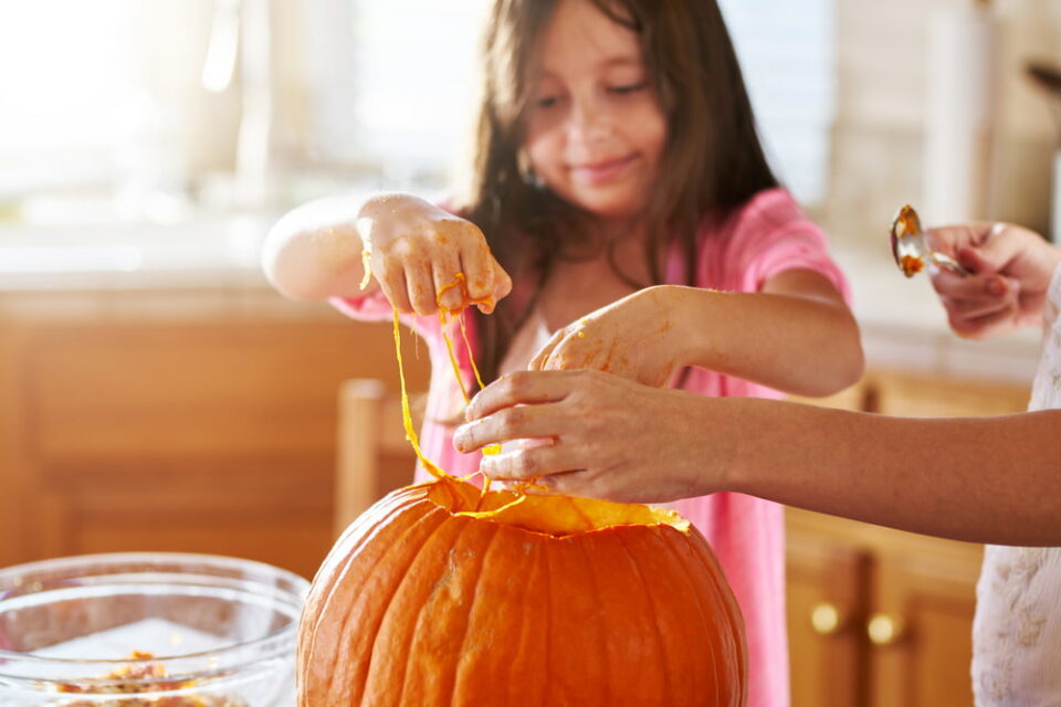 A young girl and adult remove the innards of a pumpkin together