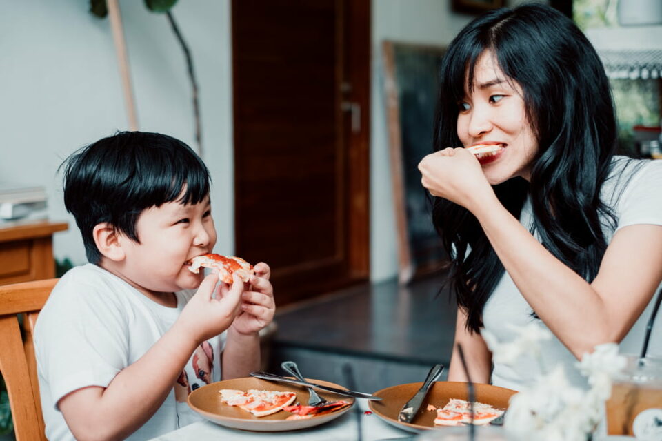 A mother and son eating homemade pizza at the table.