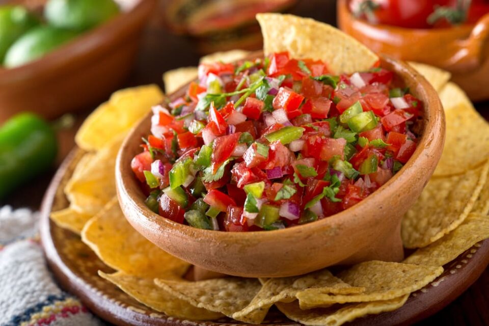 A bowl of fresh salsa surrounded by corn tortilla chips.