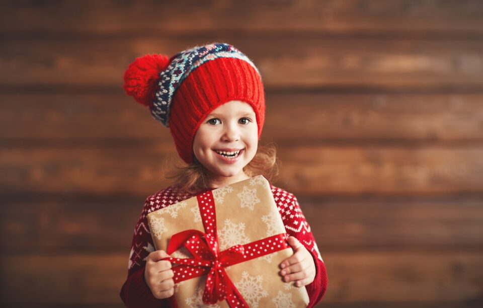 Little girl in a red hat excitedly holding a Christmas gift