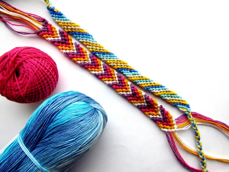 Two colorful friendship bracelets next to balls of embroidery thread.