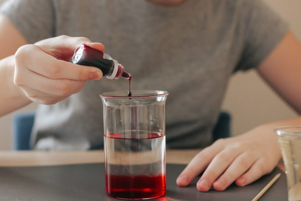 A child’s hands adding red food coloring to a glass of water.
