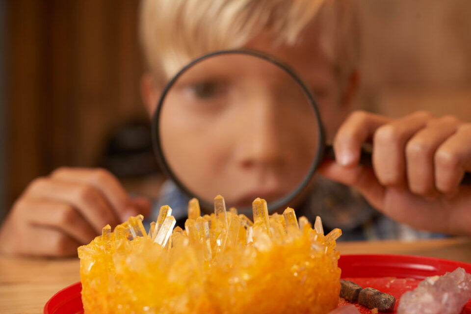 A boy looking at crystals through a magnifying glass.