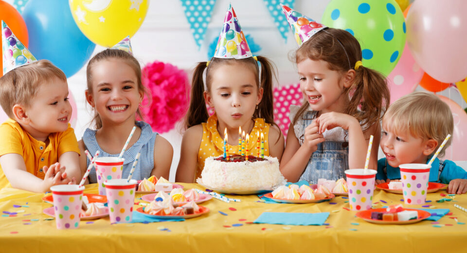 A group of kids watching a young girl blow out her birthday candles at a party
