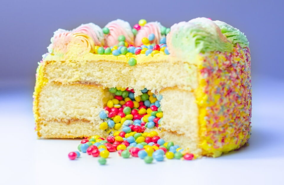 A sliced piñata cake with yellow frosting and multicolored candies spilling out from the center