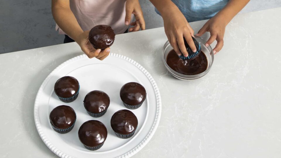 Kids glazing chocolate cupcakes.