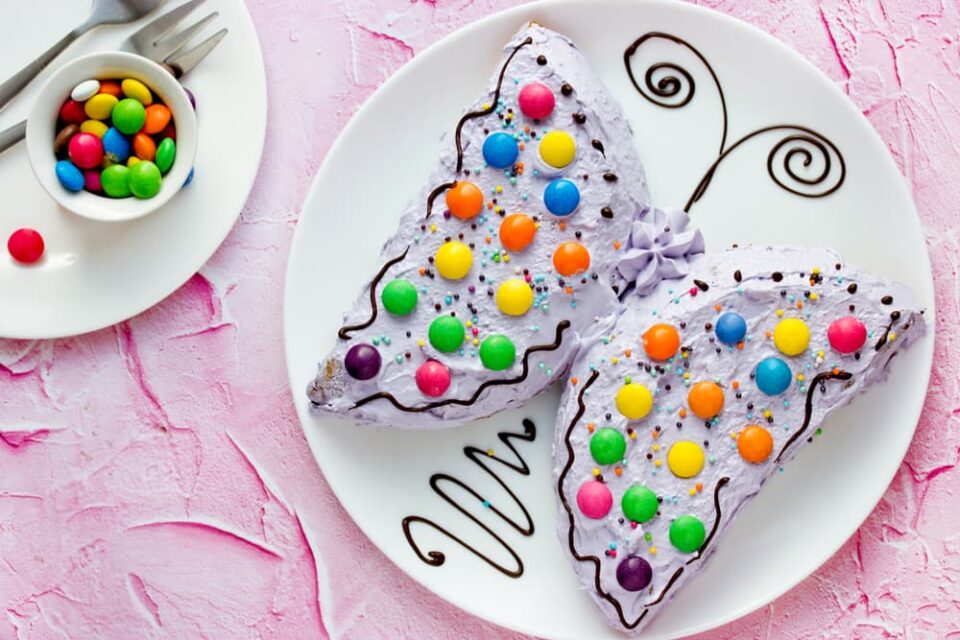 Light purple butterfly decorated with chocolate candies on a white plate