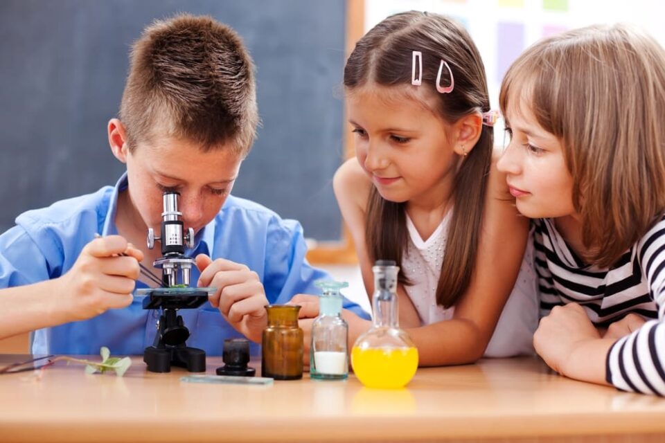 Three children gather around a microscope in a school lab.