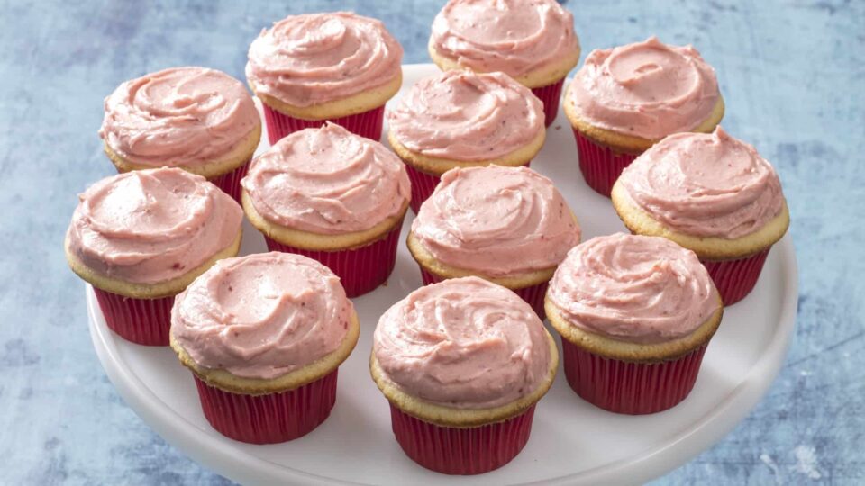 Yellow cupcakes with strawberry frosting on a white plate.