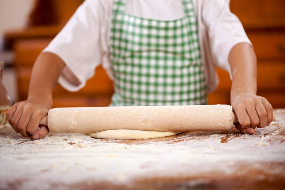 A child in a green and white checked apron rolls out dough on a counter