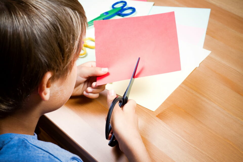 A-child-cutting-a-piece-of-red-paper-at-a-table
