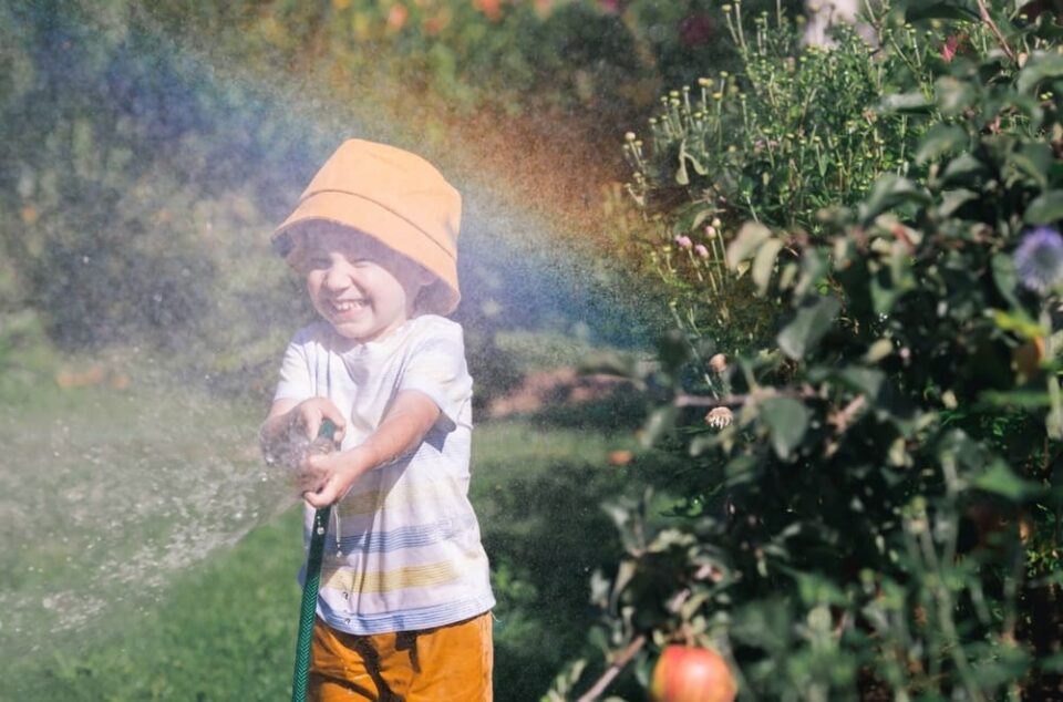 Boy-playing-with-hose-in-backyard-with-rainbow-in-front-of-him