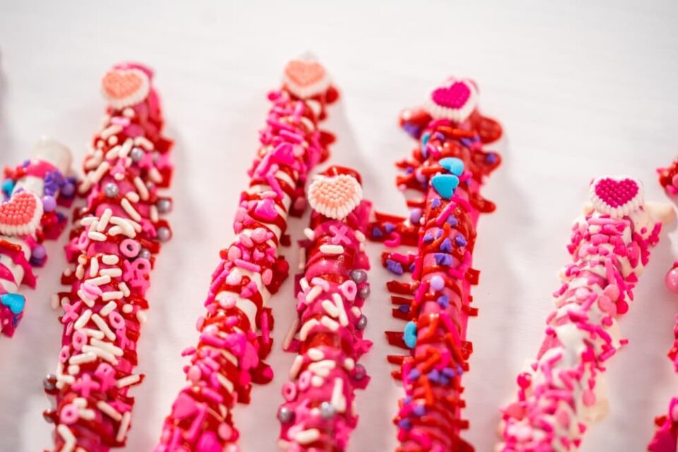 Close-up-of-pretzel-rods-covered-in-chocolate-sprinkles-and-heart-shaped-candies
