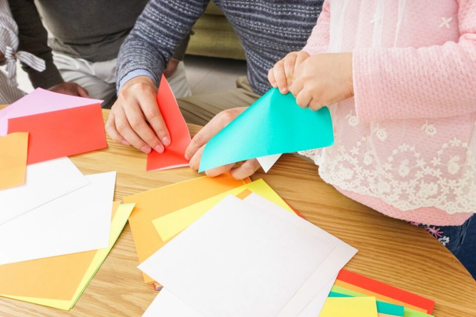 Image-of-two-childrens-hands-as-they-practice-origami-at-a-table