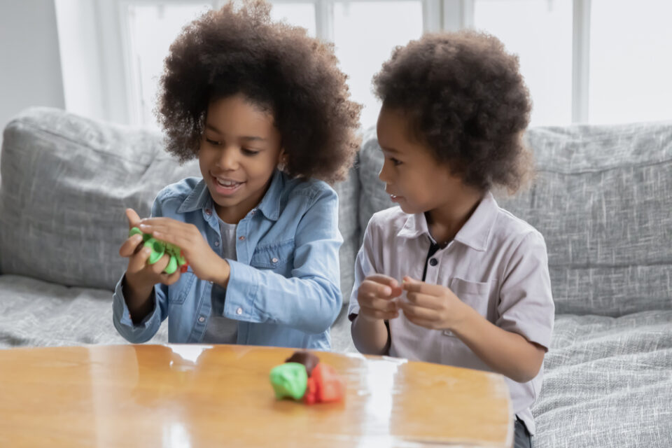 Two children play with clay while sitting at a coffee table.