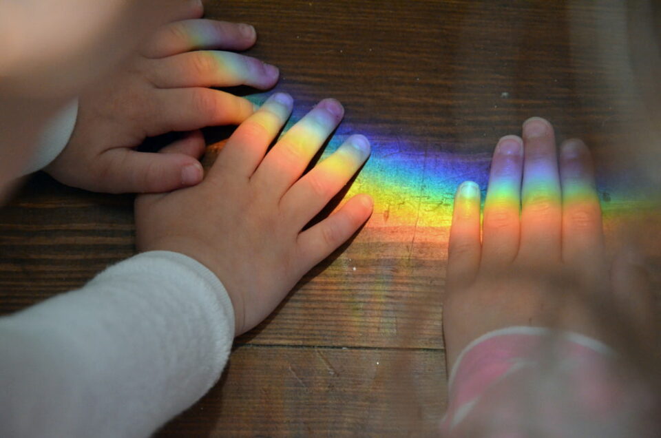 Two-children-put-their-hands-on-rainbow-reflected-on-table