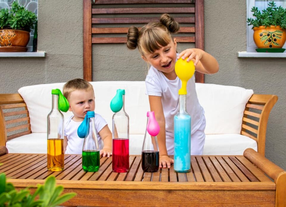 Two-children-testing-balloon-experiment-with-multiple-bottles-and-colored-vinegar