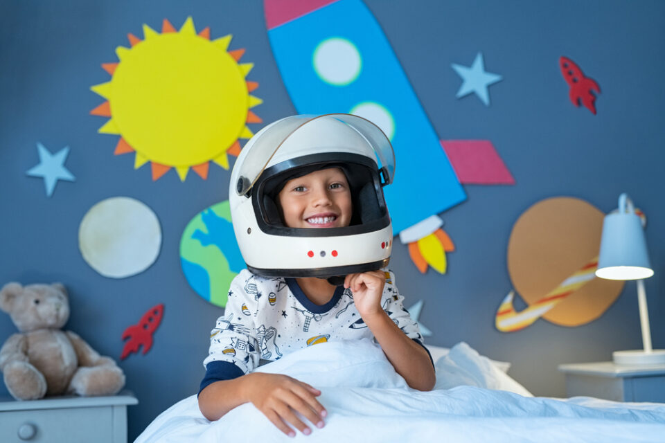 A boy wearing an astronaut helmet in a space-themed room.
