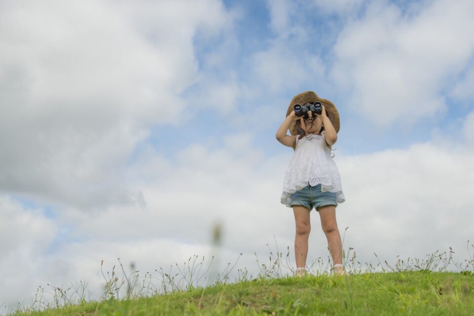 A girl looking through binoculars at the blue sky.