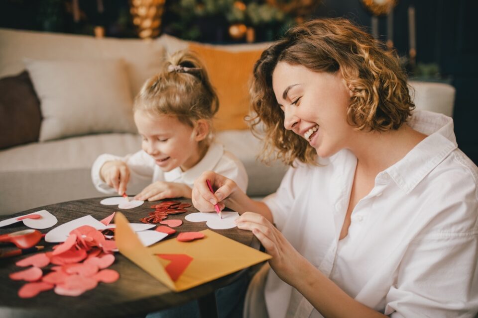 A mother and daughter cutting out paper hearts for a homemade Valentine’s Day gift.